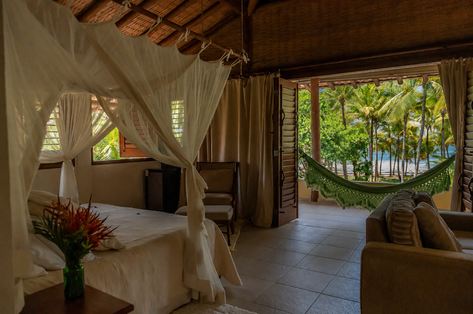 Suíte master com cama de dossel e varanda com rede e vista para o mar